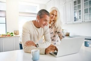 Elderly retired couple exploring financial planning and reverse mortgage options on a laptop in a bright sunny kitchen in Ontario - Mortgage Scout