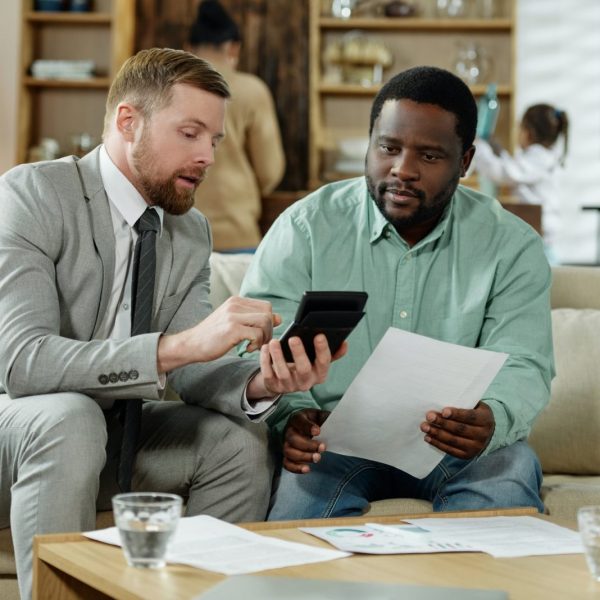 Man with adviser calculating mortgage rate in home, family in the background, Ontario mortgage services - Mortgage Scout